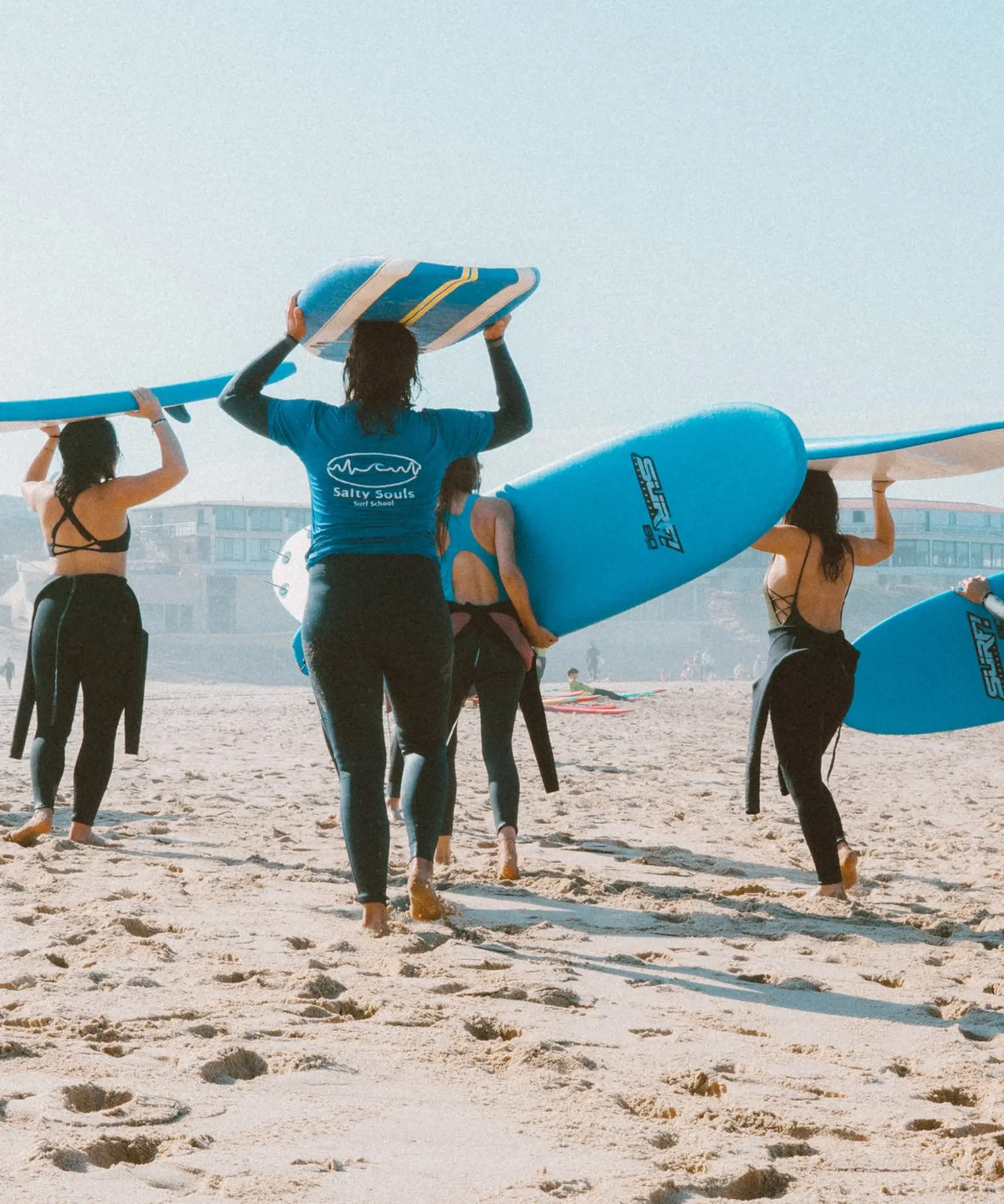 A group of people walking along a sandy beach with surf boards.