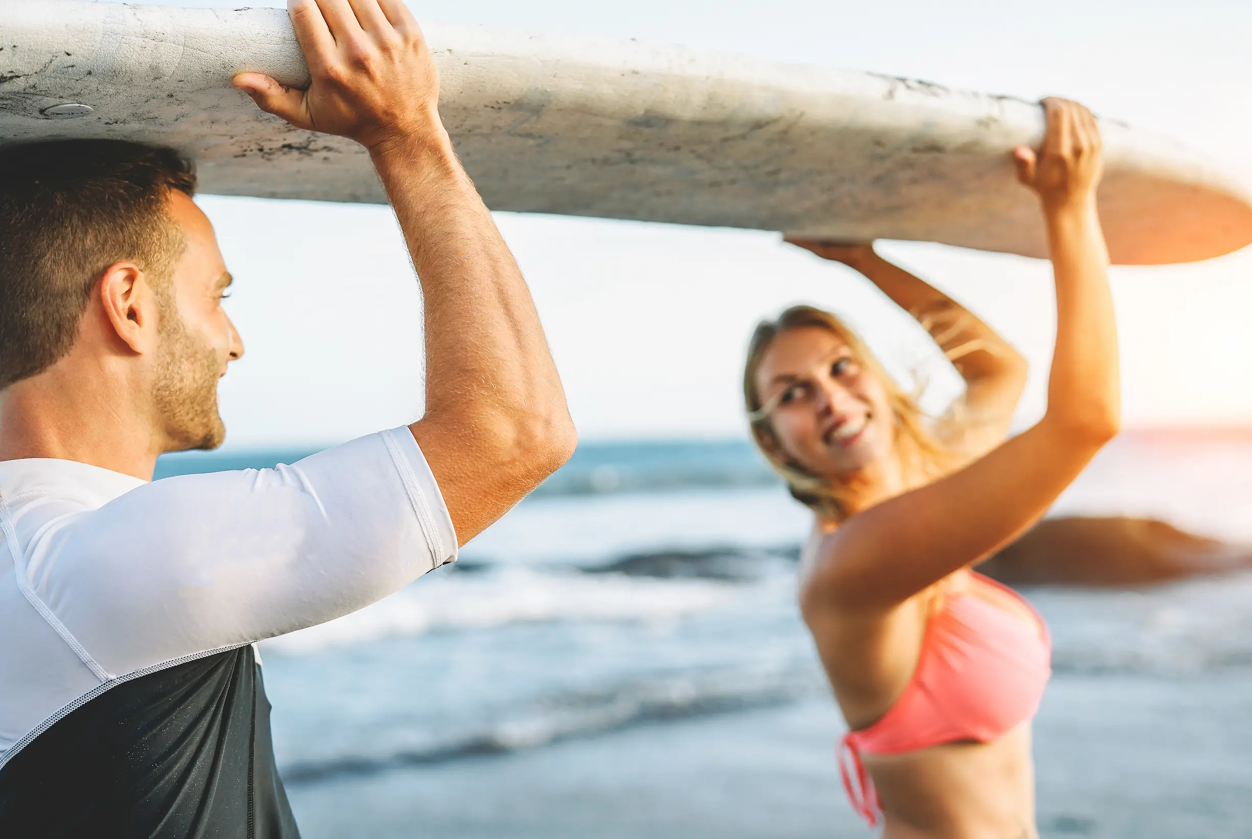 male and female couple holding up a surf board in the ocean