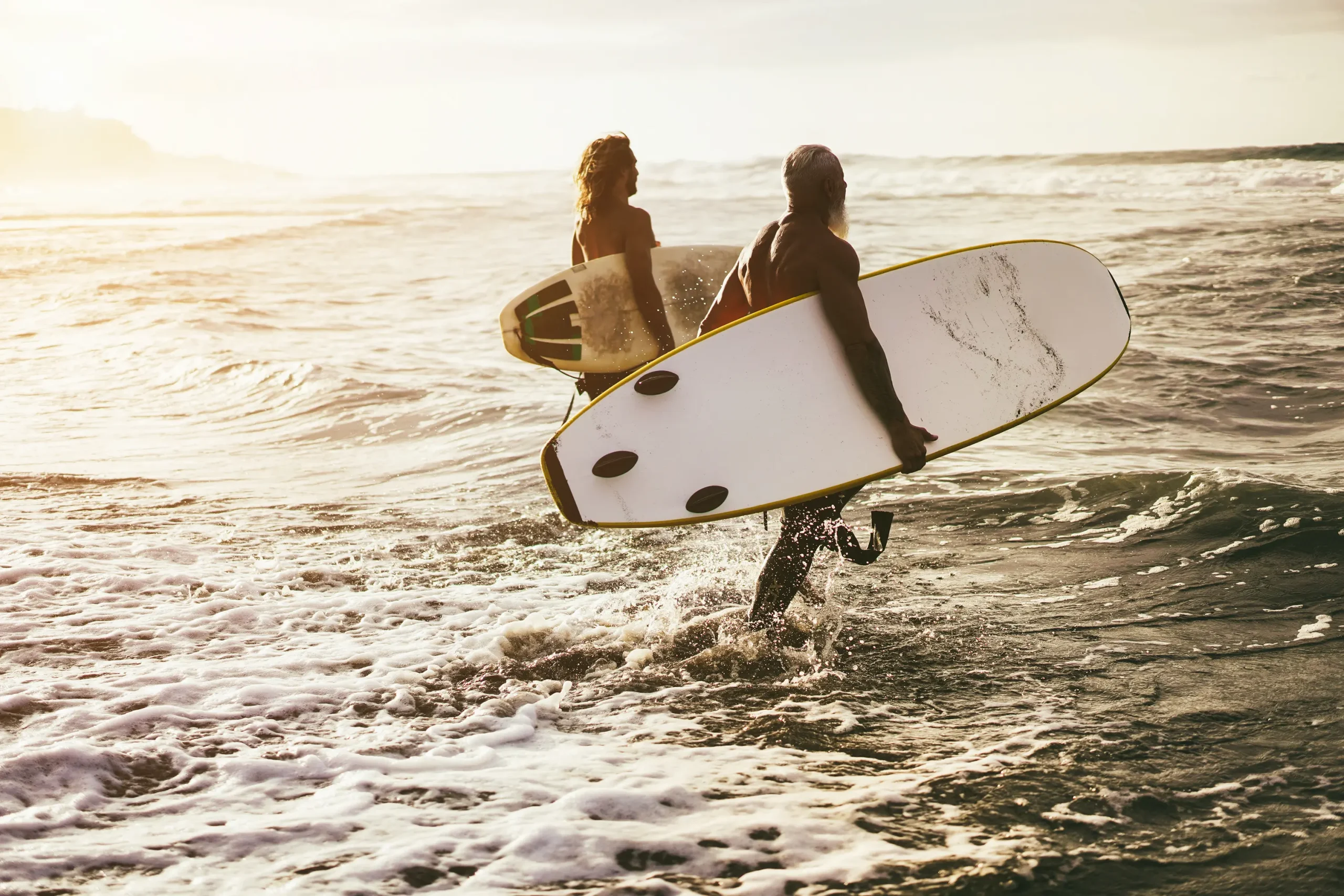 Two men walking into the ocean with surf boards.